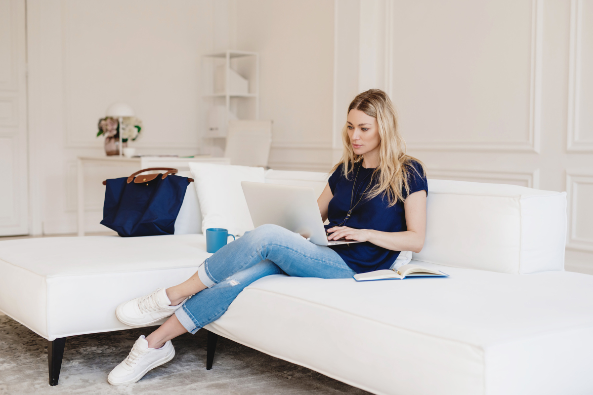 Why coaches need a website Blonde woman sitting on white sofa, typing on her laptop.