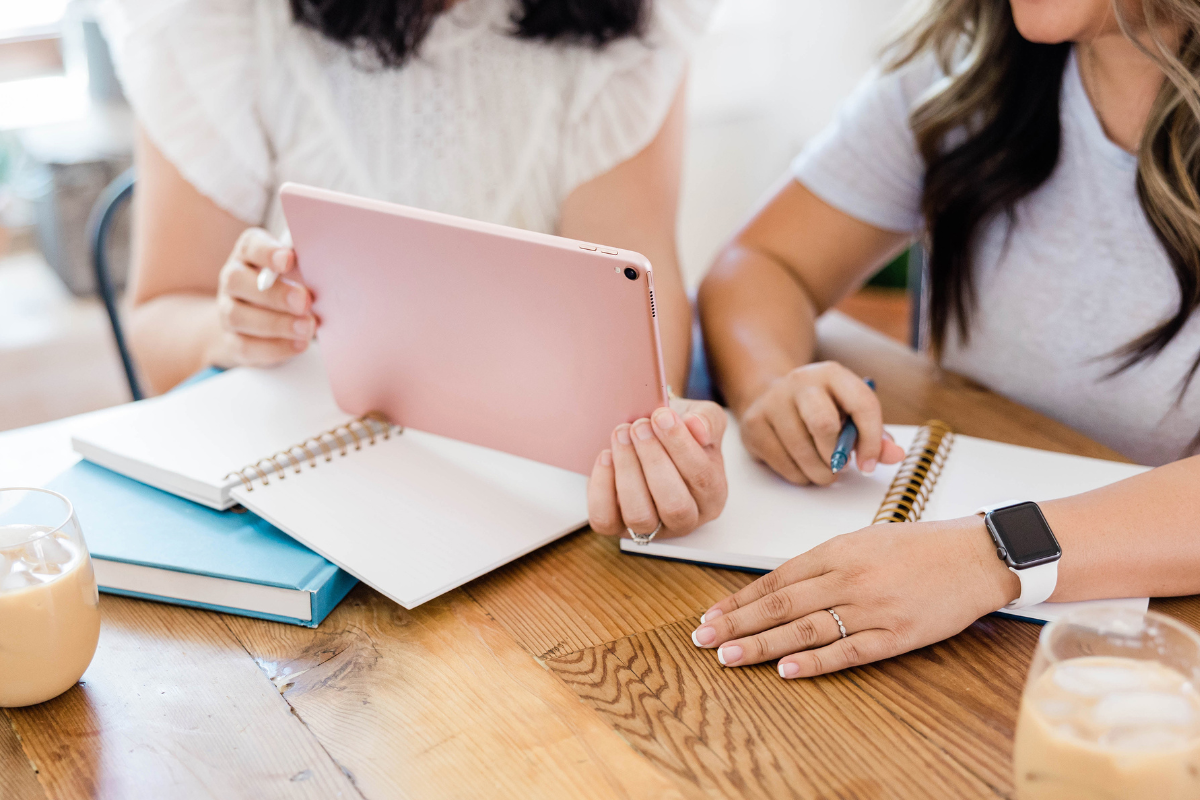 Two women sitting at a table and looking at an iPad together.